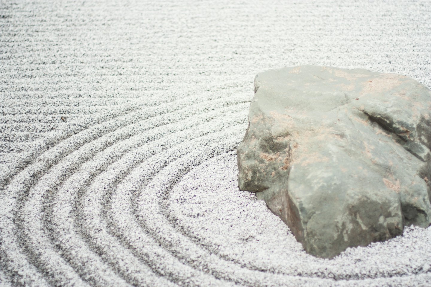 Ghiaia da giardino zen con motivi circolari e una grossa roccia.
