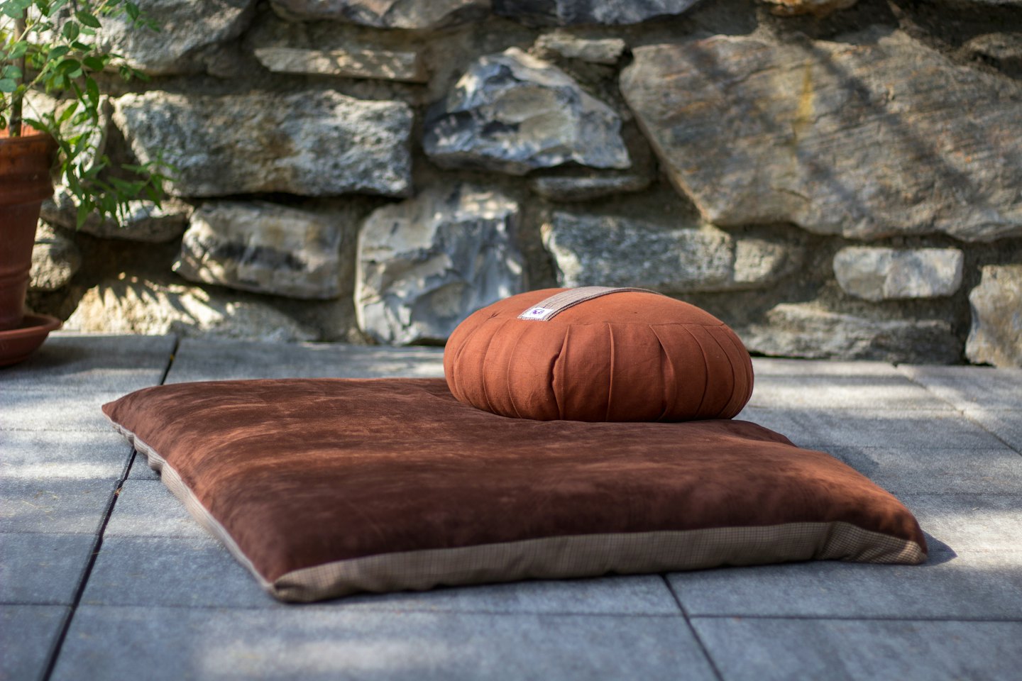 Cuscini da meditazione su un patio accanto a un muro di pietra.