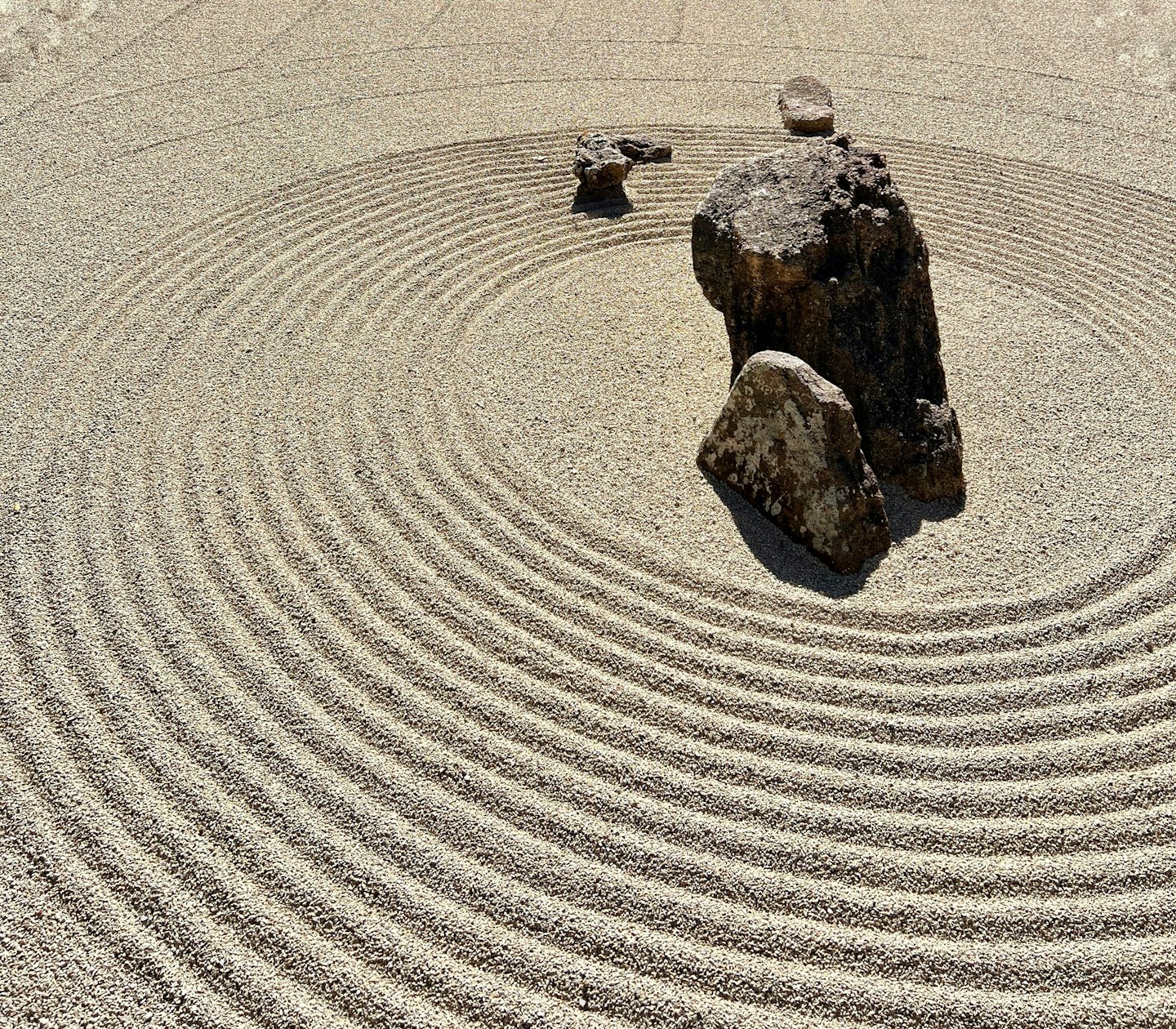 Cerchi di sabbia beige rastrellata circondano rocce scure in un giardino zen.